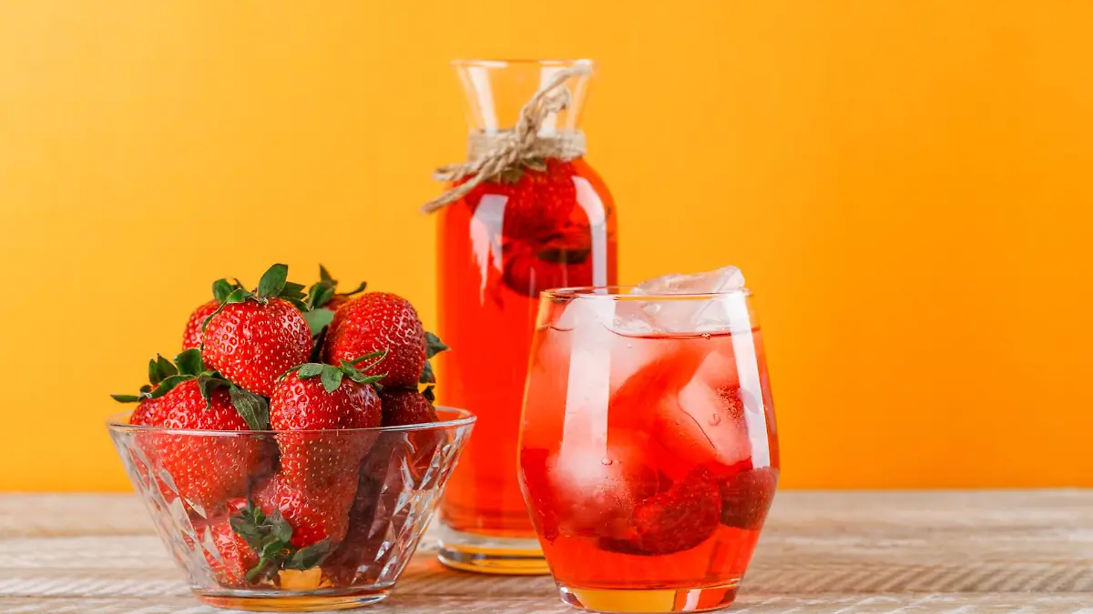 Lemonade with strawberries in jug and glass on wooden and yellow background, side view.
