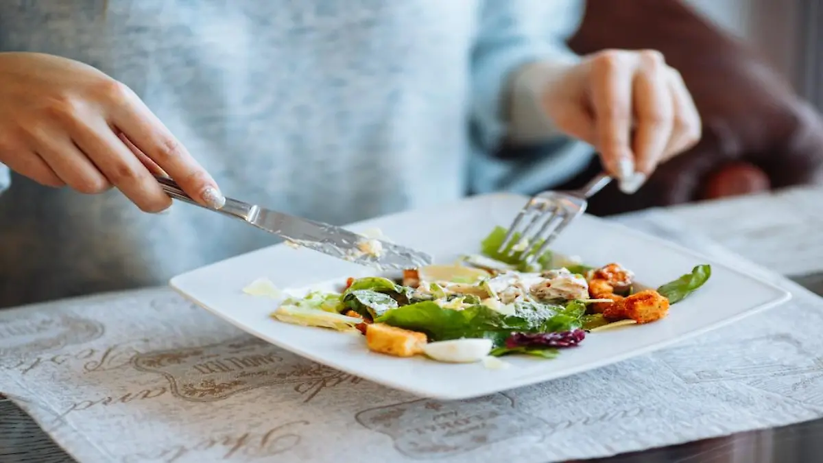 Woman's hands with Caesar salad on table in restaurant