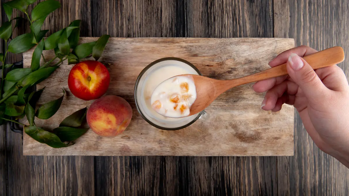top view of yogurt in a glass with wooden spoon and fresh ripe peaches on wooden board on rustic background