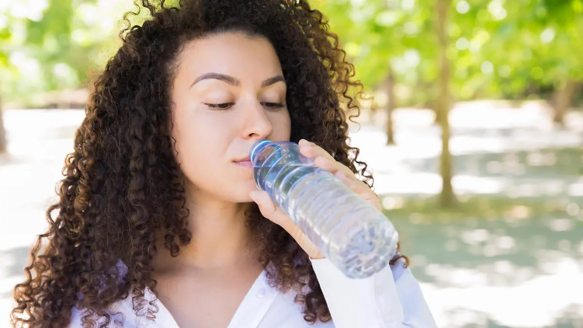 Pretty young woman drinking water from bottle in park