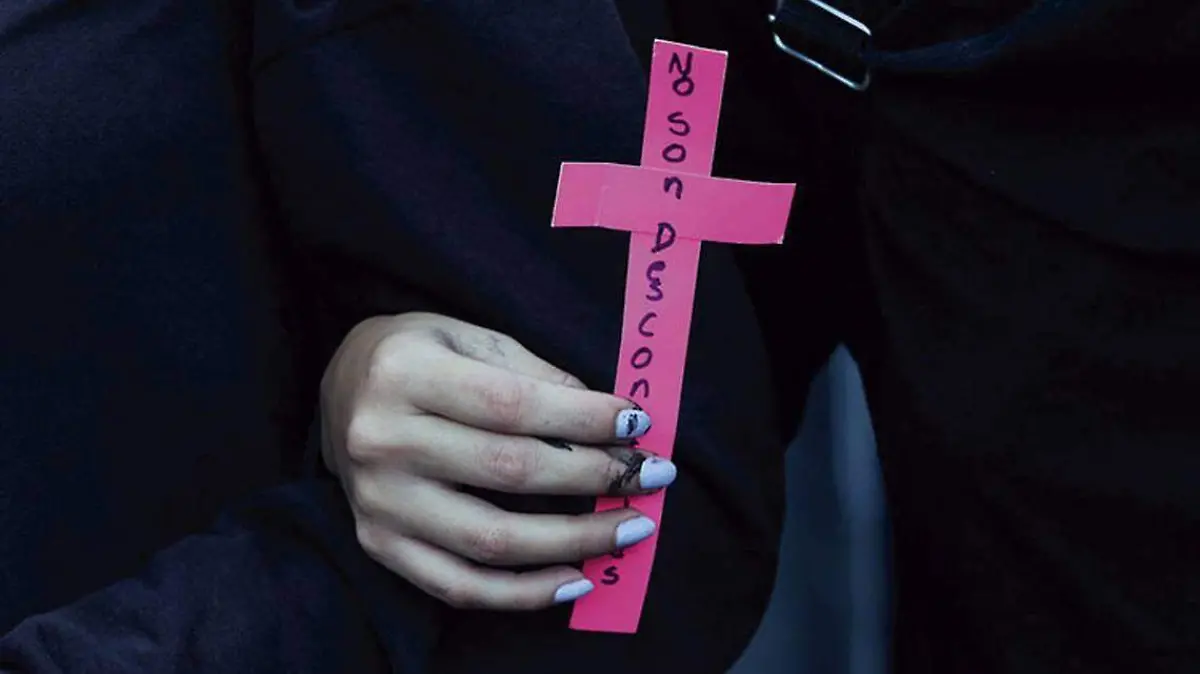 Mano de mujer sostiene una cruz de papel color rosa