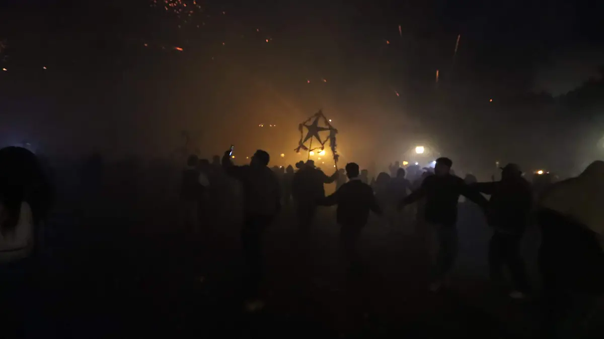 Cientos de jóvenes frente a la parroquia bailan y esquivan los cohetes que les lanzan.