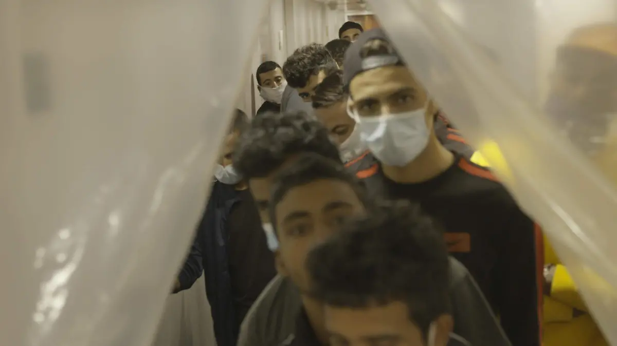 Migrants line up in close quarters waiting for their temperatures to be taken