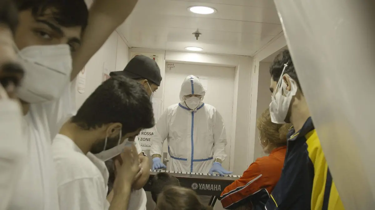 Migrants watch as Francesco plays piano in a hazmat suit