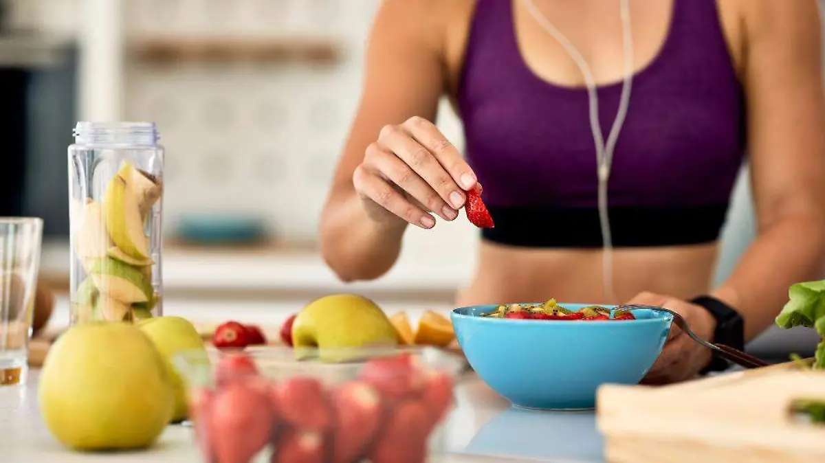 primer-plano-mujer-atletica-agregando-fresas-mientras-hace-ensalada-frutas-cocina