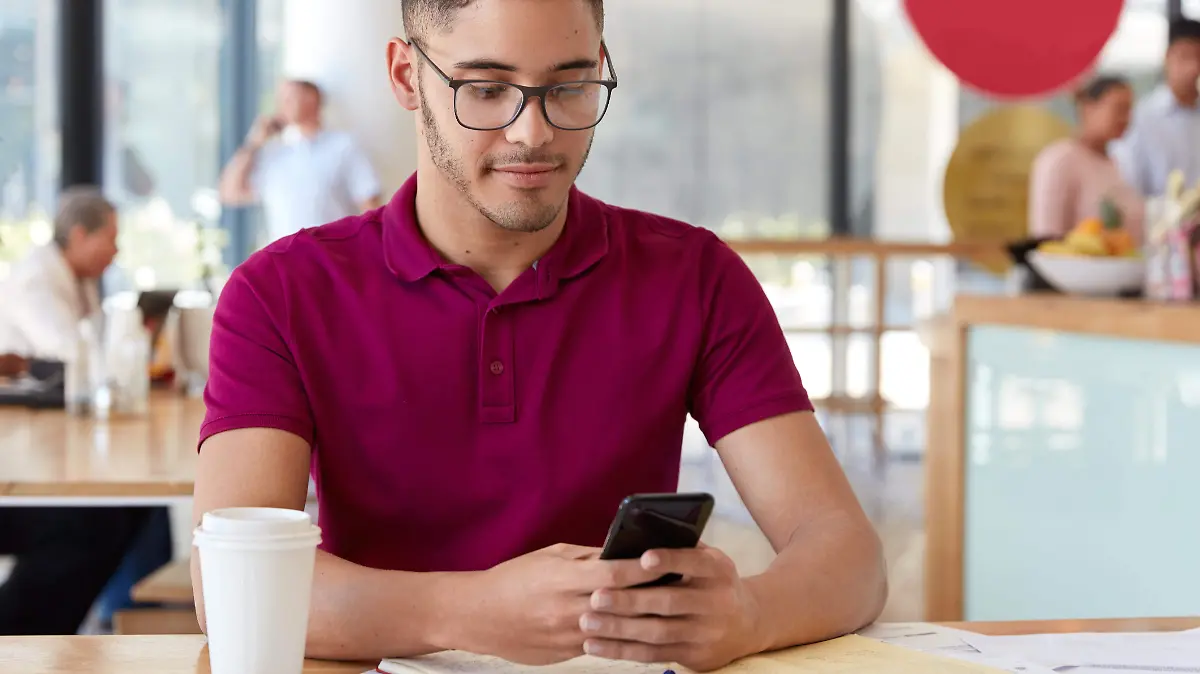 image-stylish-young-man-holds-mobile-phone-recieves-income-notification-checks-email-box-connected-high-speed-internet-wears-optical-glasses-develops-reasearch-project-makes-home-assignment