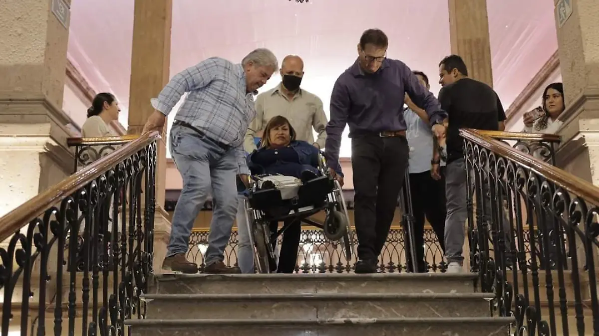 Personas cargando a una mujer en silla de ruedas