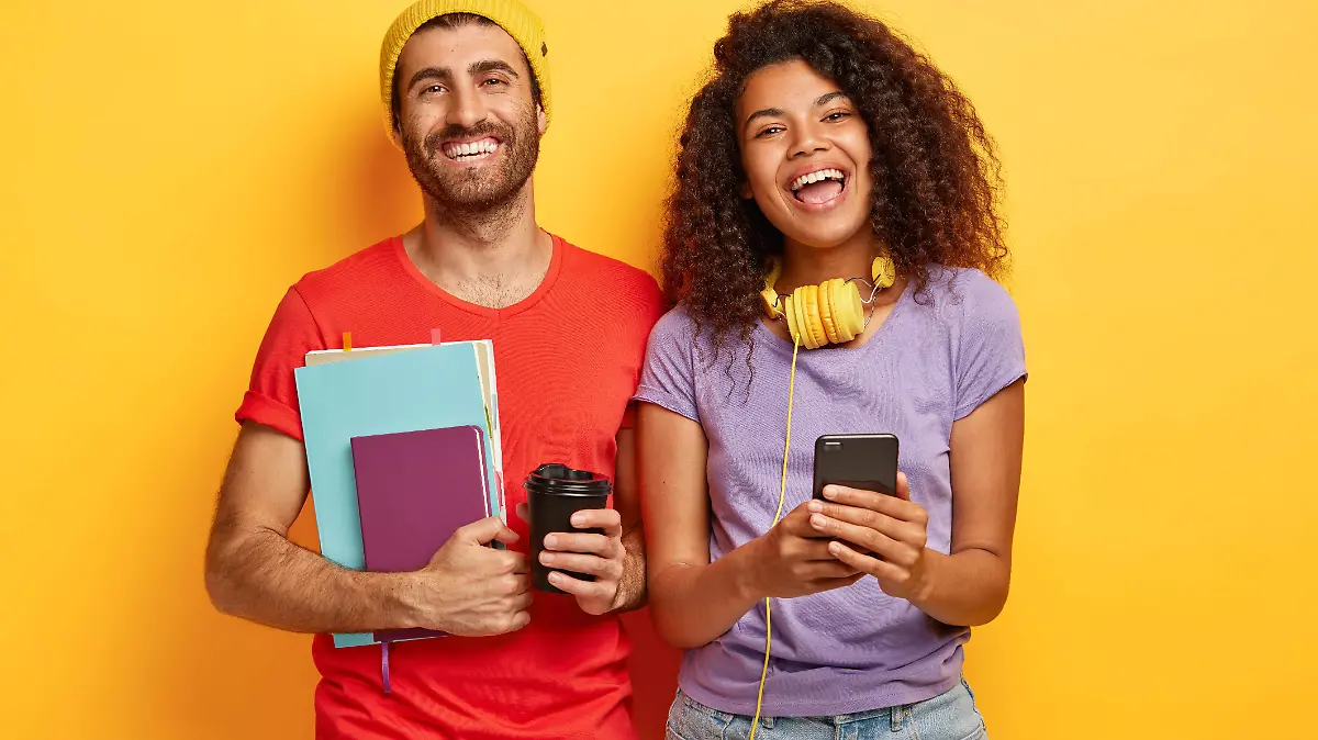 happy-stylish-couple-posing-against-the-yellow-wall-with-gadgets