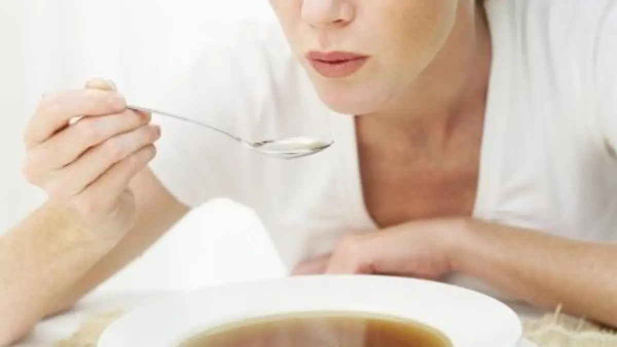 Young woman blowing a spoonful of hot soup