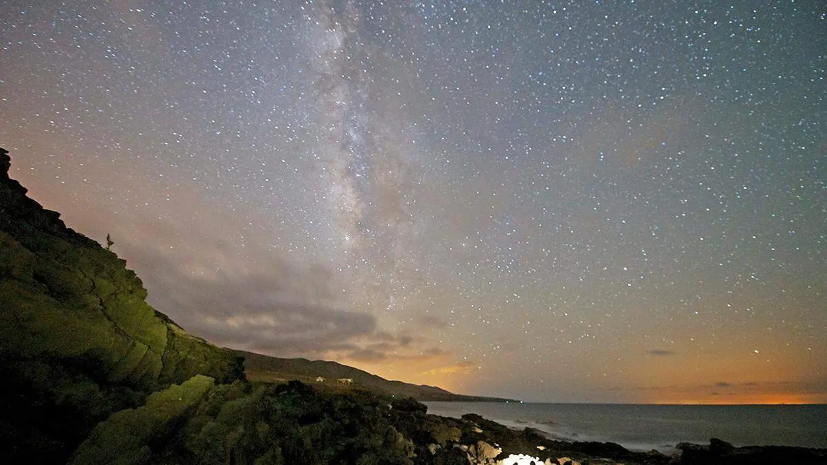 Una playa con el cielo iluminado por la presencia de estrellas, planetas y demás