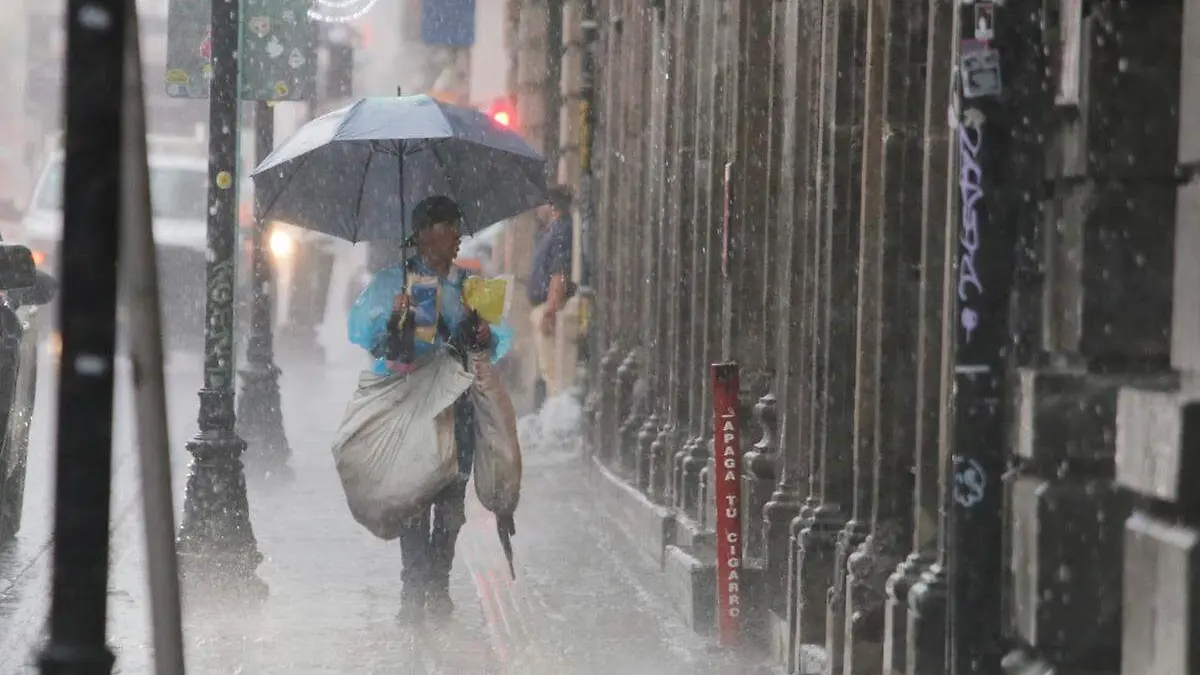 persona se protege con un paraguas de fuerte lluvia en el zocalo de Puebla