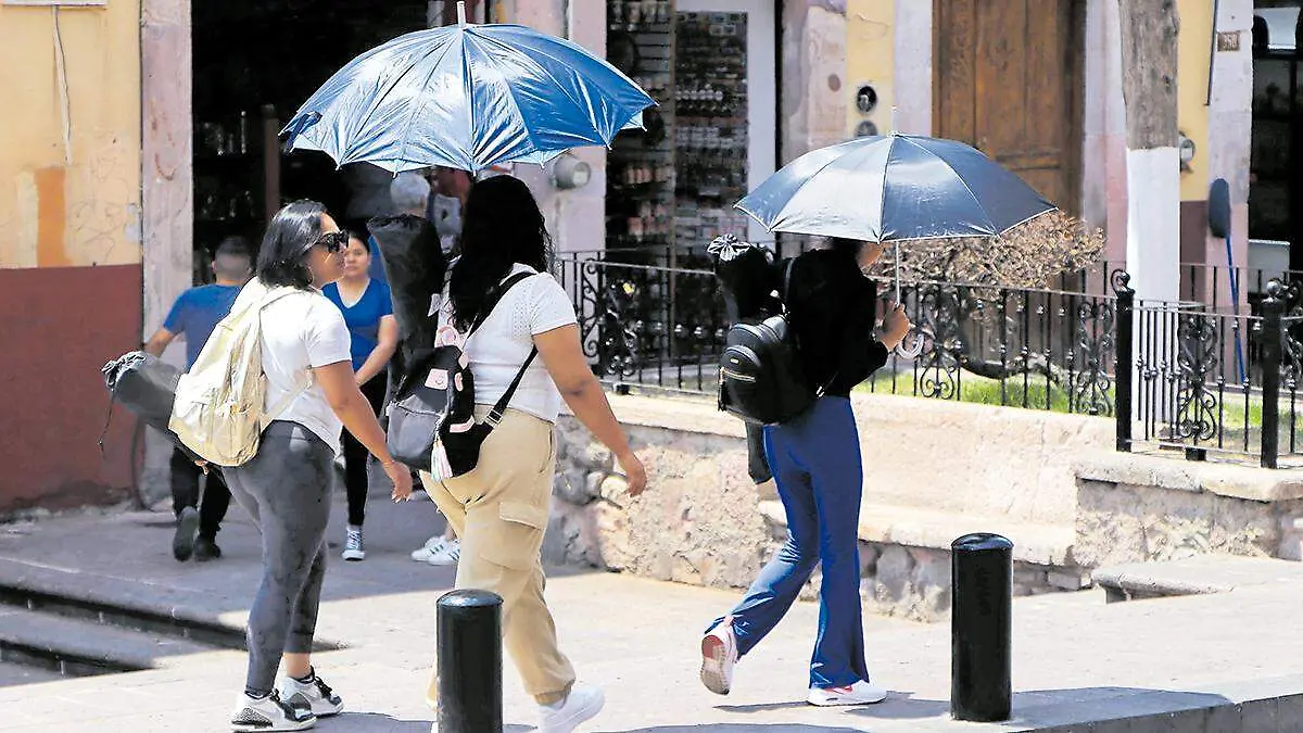 Mujeres se cubren de los rayos solares con sombrillas en Zacatecas