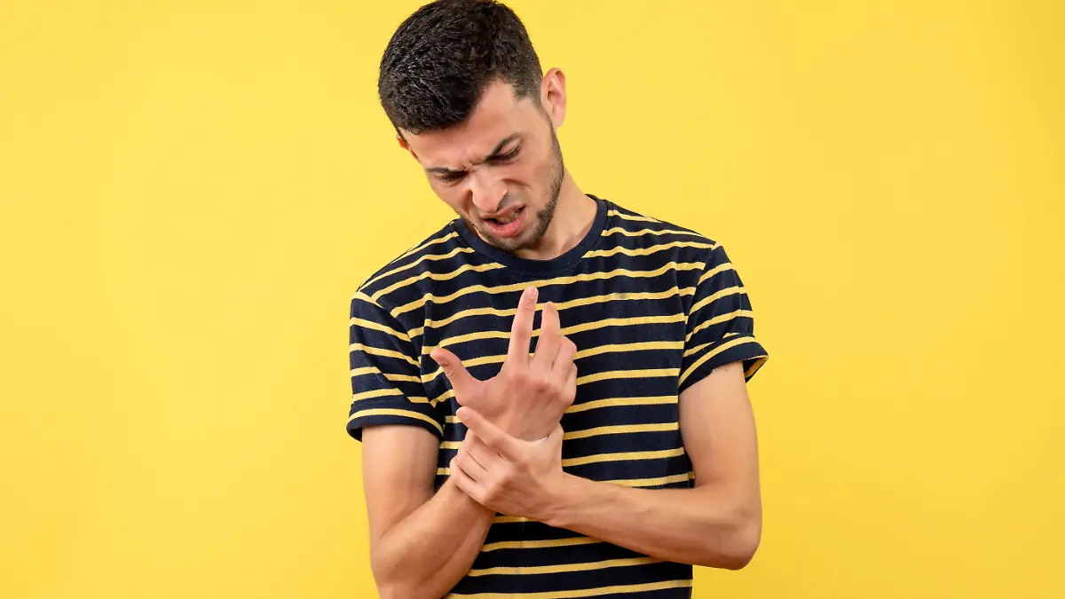 vista-frontal-joven-camiseta-rayas-blanco-negro-sosteniendo-mano-dolor-sobre-fondo-amarillo-aislado