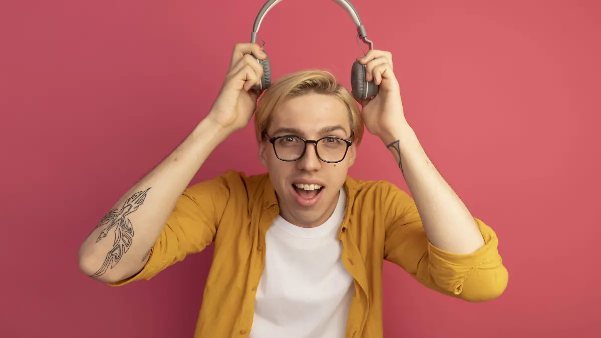 chico-rubio-joven-alegre-camiseta-amarilla-gafas-poniendo-auriculares-cabeza-aislada-rosa