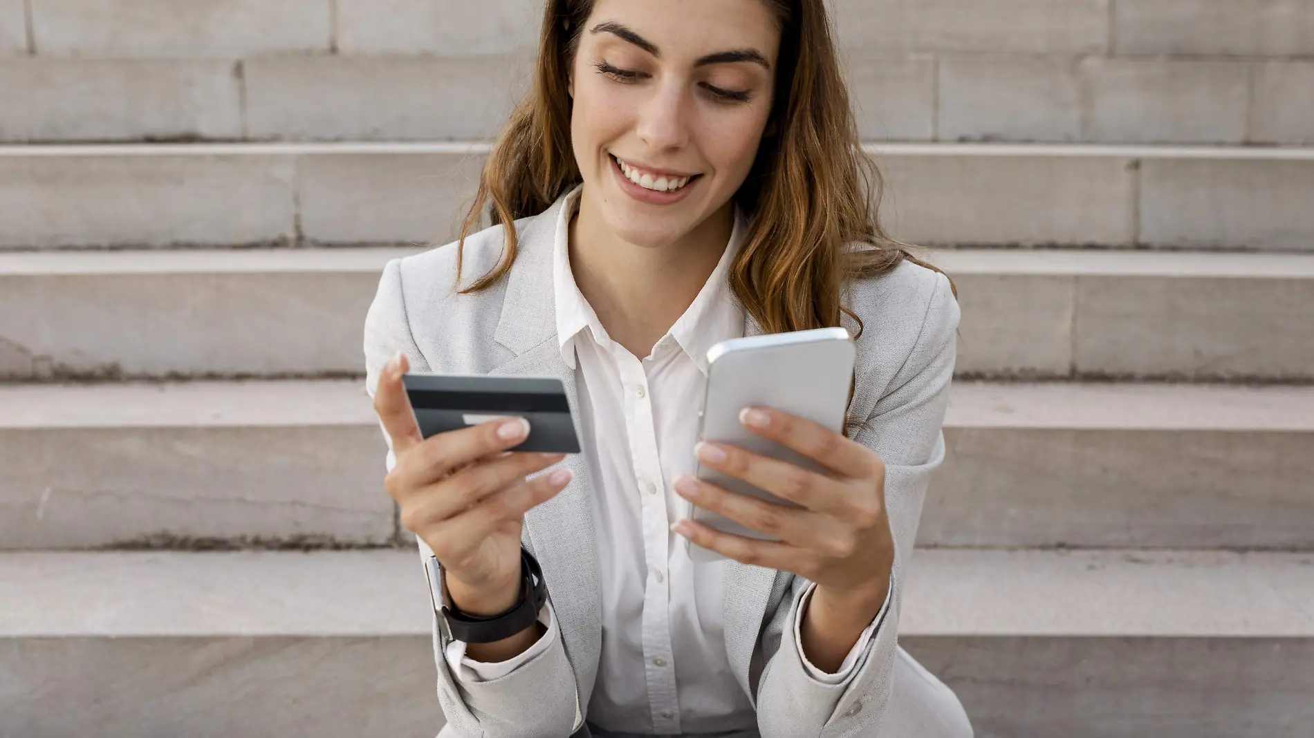 businesswoman-shopping-online-with-smartphone-and-credit-card-while-sitting-on-stairs