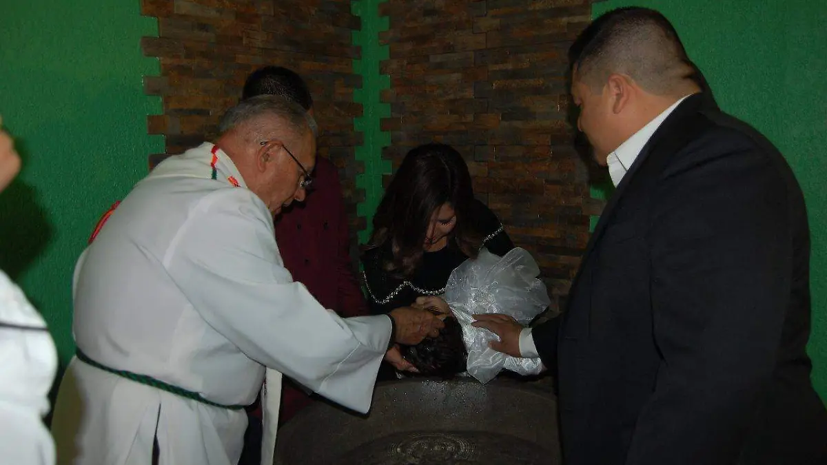 En la pila bautismal papás y padrinos.